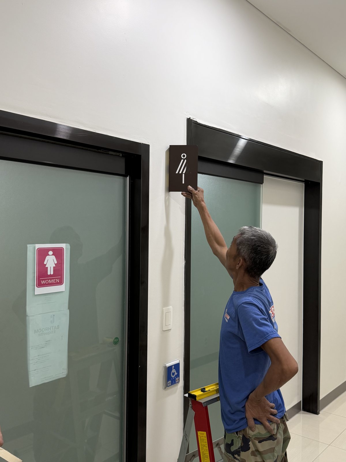 Installer mounting a restroom sign above a door