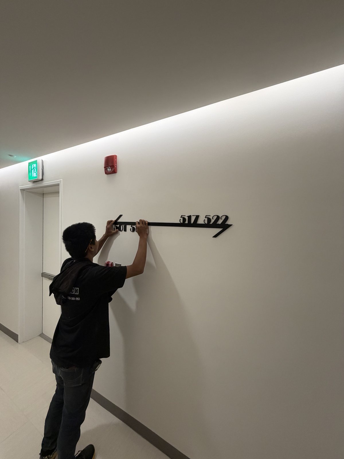 Wiltech installer fixing a room-range directional along a First Clark corridor